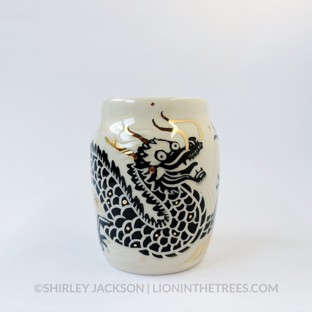 Large sgraffito vessel done with black underglaze featuring a dragon motif that curls around the entire vessel. There are also gold overglaze details throughout the piece.