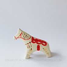 Horse totem done with red underglaze that create the bridle and saddle, finished with clear glaze and gold overglaze details.