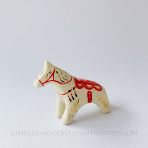 Horse totem done with red underglaze that create the bridle and saddle, finished with clear glaze and gold overglaze details.