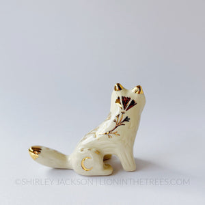 White wolf totem in a sitting position done with black underglaze, finished with clear glaze and gold overglaze details.