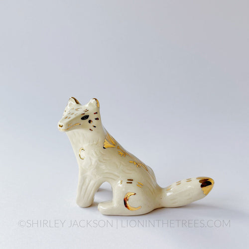 White wolf totem in a sitting position done with black underglaze, finished with clear glaze and gold overglaze details.