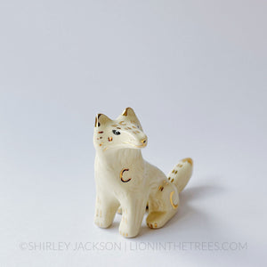 White wolf totem in a sitting position done with black underglaze, finished with clear glaze and gold overglaze details.